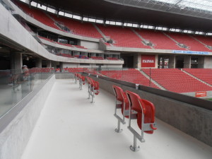 Foto da área para pessoa em cadeira de rodas. Vemos alguns assentos vermelhos para acompanhantes e espaços livres que serão ocupados por cadeirantes.
